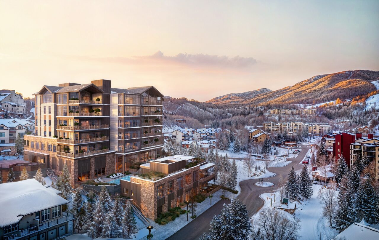 A modern building surrounded by snow-covered trees and mountains, with a sunset sky in the background.